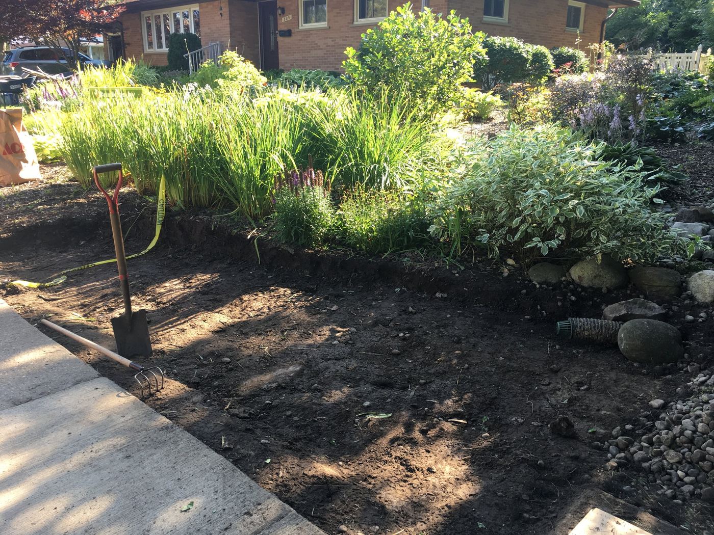 Rain garden bed before expansion, freshly dug along the river-rock border