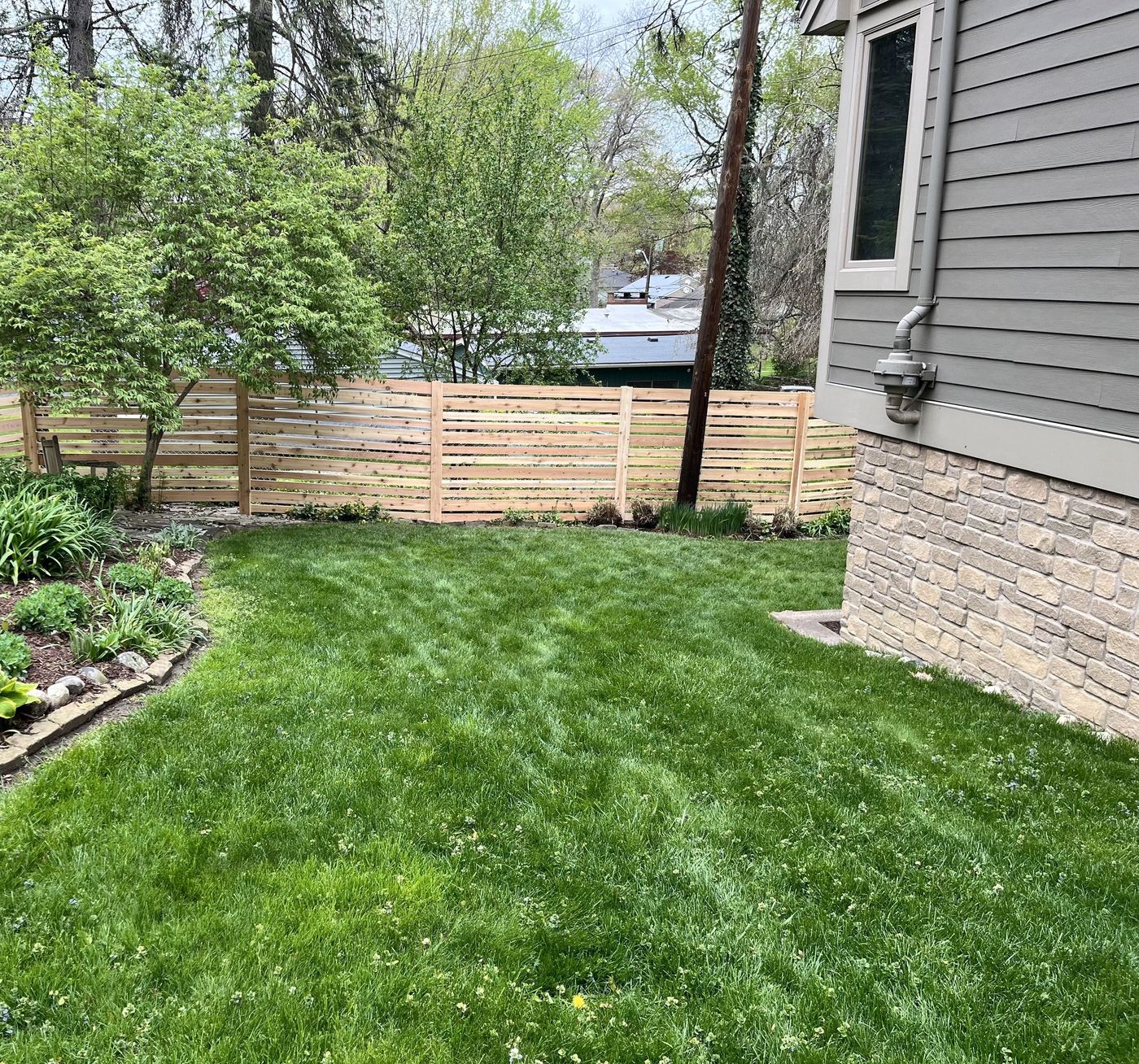 Cedar horizontal-slat privacy fence against stone-veneer home